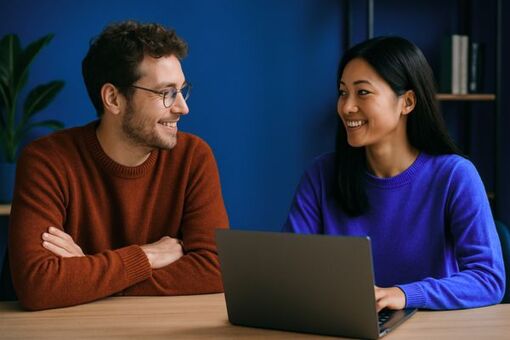 Zwei Personen sitzen gemeinsam am Tisch mit Laptop und führen ein Gespräch im modernen Büro
