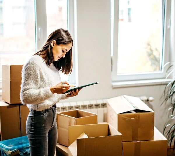 Junge Frau steht zwischen Umzugskartons und schaut auf ihr Smartphone, Symbol für einfache Organisation und geprüfte Hilfe beim Umzug mit KnowS.