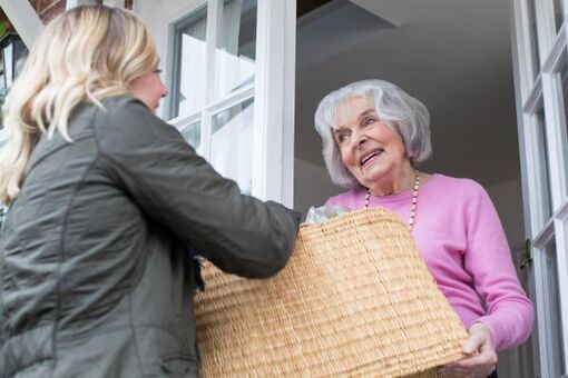 Young woman presents an elderly lady with a basket – a symbol of mutual aid and neighborhood support via KnowS in Switzerland.