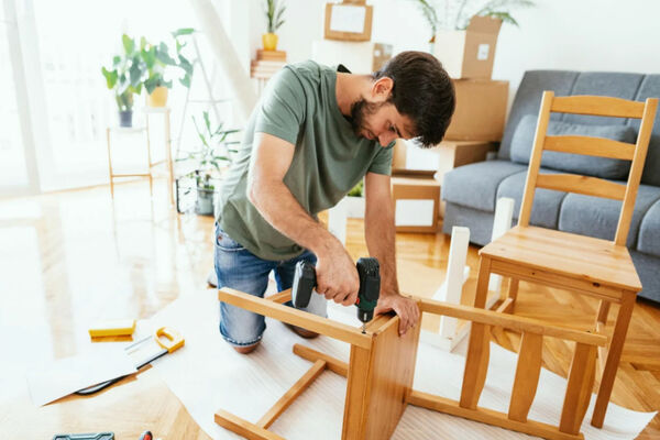 A handyman assembling furniture with a cordless drill in an apartment.