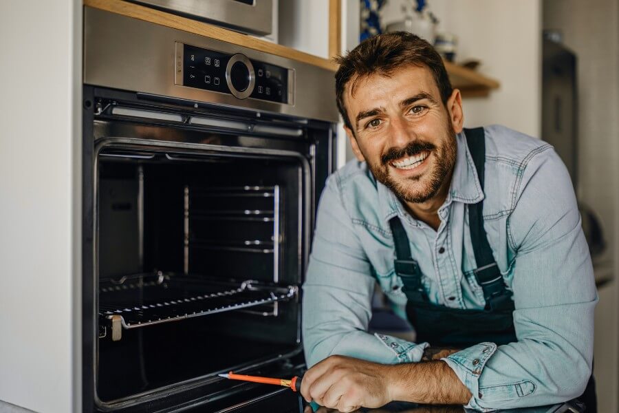 Handwerker arbeitet am Ofen und lächelt in die Kamera