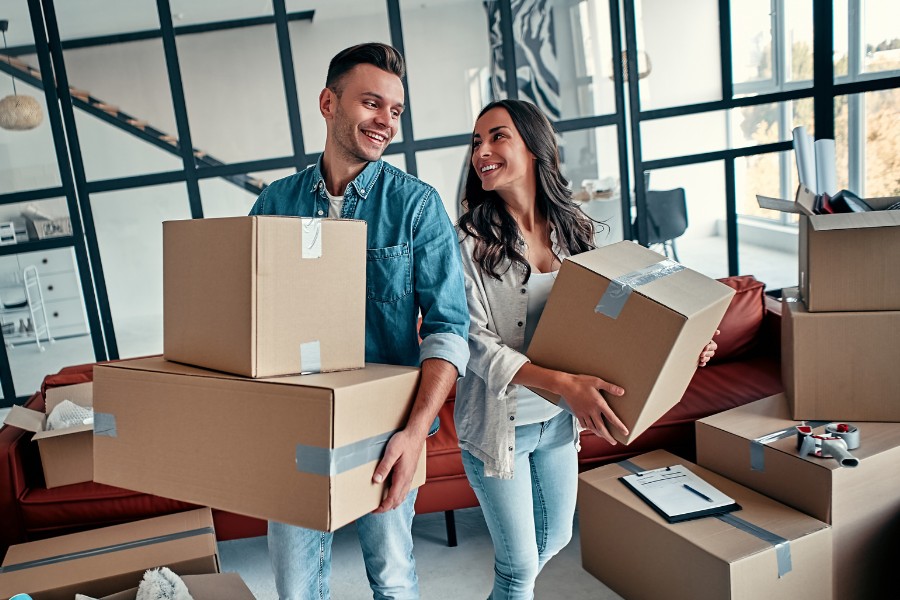 Junges Paar trägt Umzugskartons in eine neue Wohnung, Symbol für Unterstützung und stressfreien Umzug mit geprüften Helfern über KnowS.