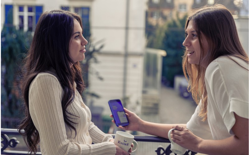 KnowS App - Menschen finden Unterstützung und Aufträge in ihrer Nähe Zwei Personen unterhalten sich draussen, eine zeigt die KnowS App auf dem Smartphone – Plattform für Aufträge und Hilfe in der Schweiz